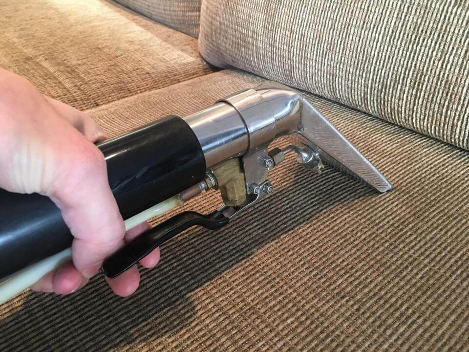 beige couch being cleaned with a metal upholstery tool