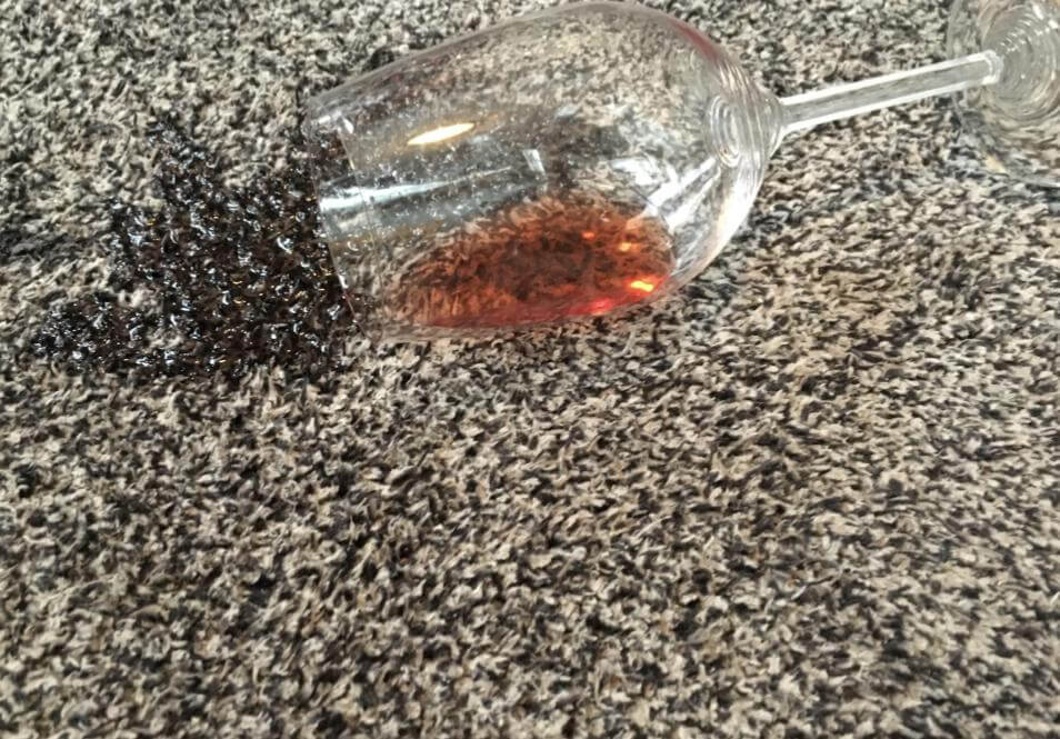 glass of spilled red wine on grey carpet