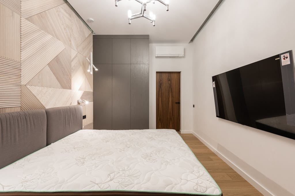 Interior of modern light hotel room with TV on wall near bed and cabinet near door